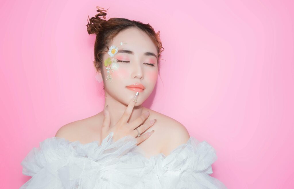 A serene portrait of a woman with floral face makeup against a vibrant pink background, exuding calmness.