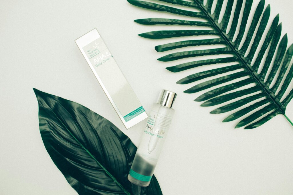Top view composition of cosmetic products placed on white desk near fresh tropical green leaves