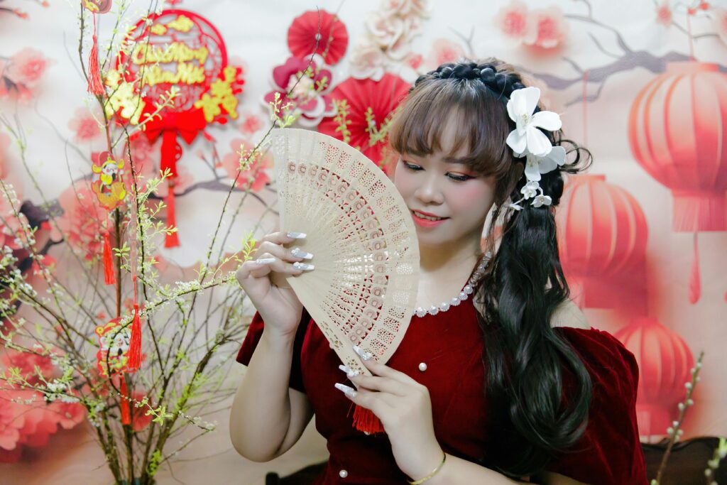 Woman in traditional dress with fan during vibrant Lunar New Year celebration.