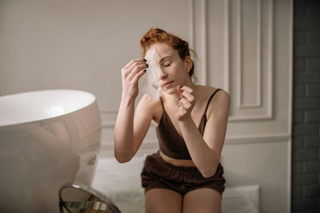 A woman engages in self-care by applying a cosmetic face mask in a stylish bathroom setting.