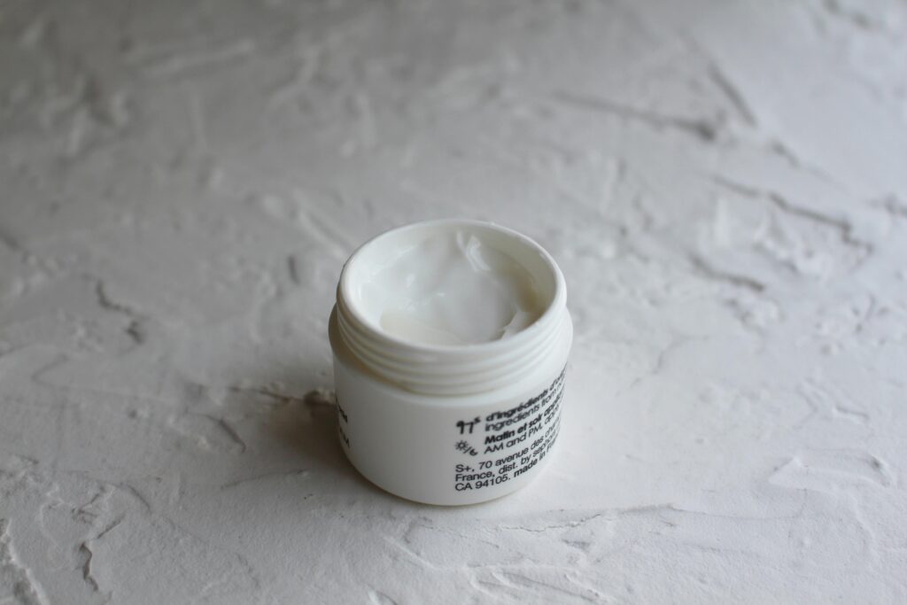 A jar of face cream on a textured surface, perfect for skincare advertising.