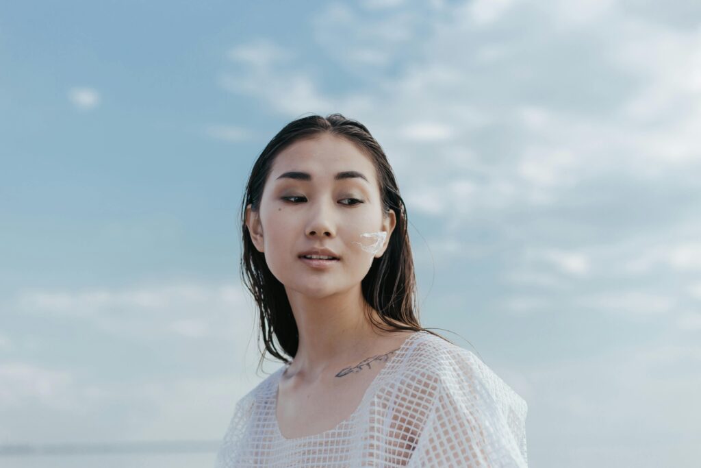 Portrait of an Asian woman outdoors with natural makeup, in soft lighting under a blue sky.