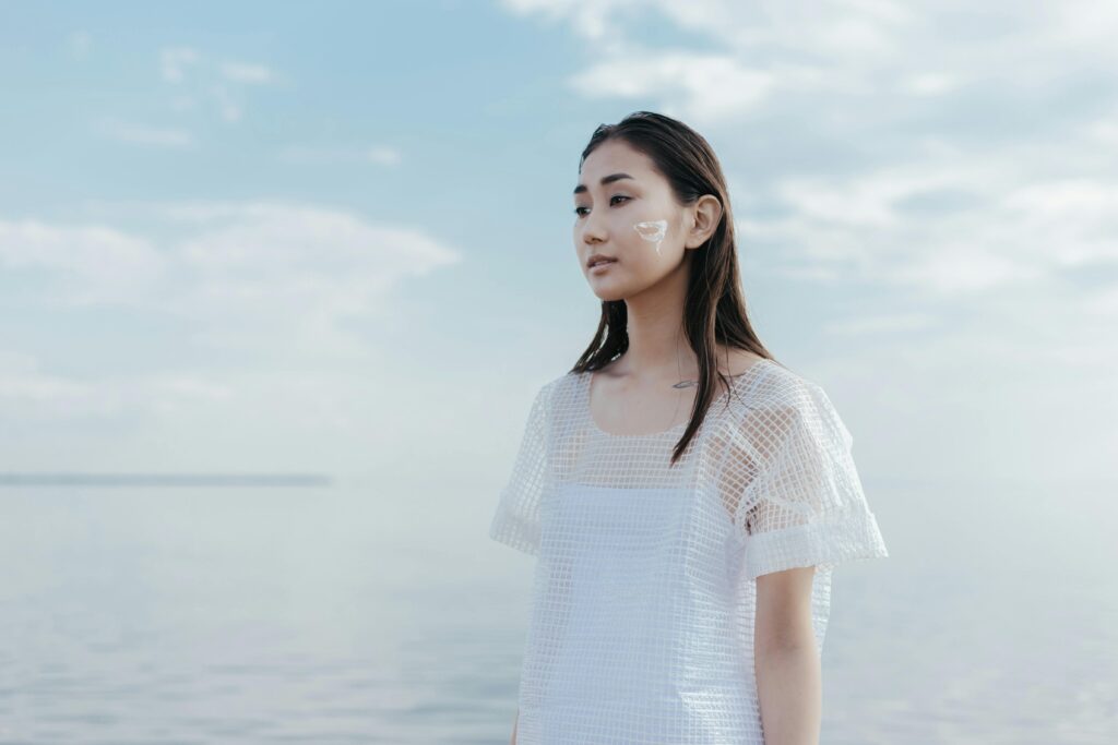 A tranquil portrait of a woman in white by the ocean with face paint for a conceptual look.